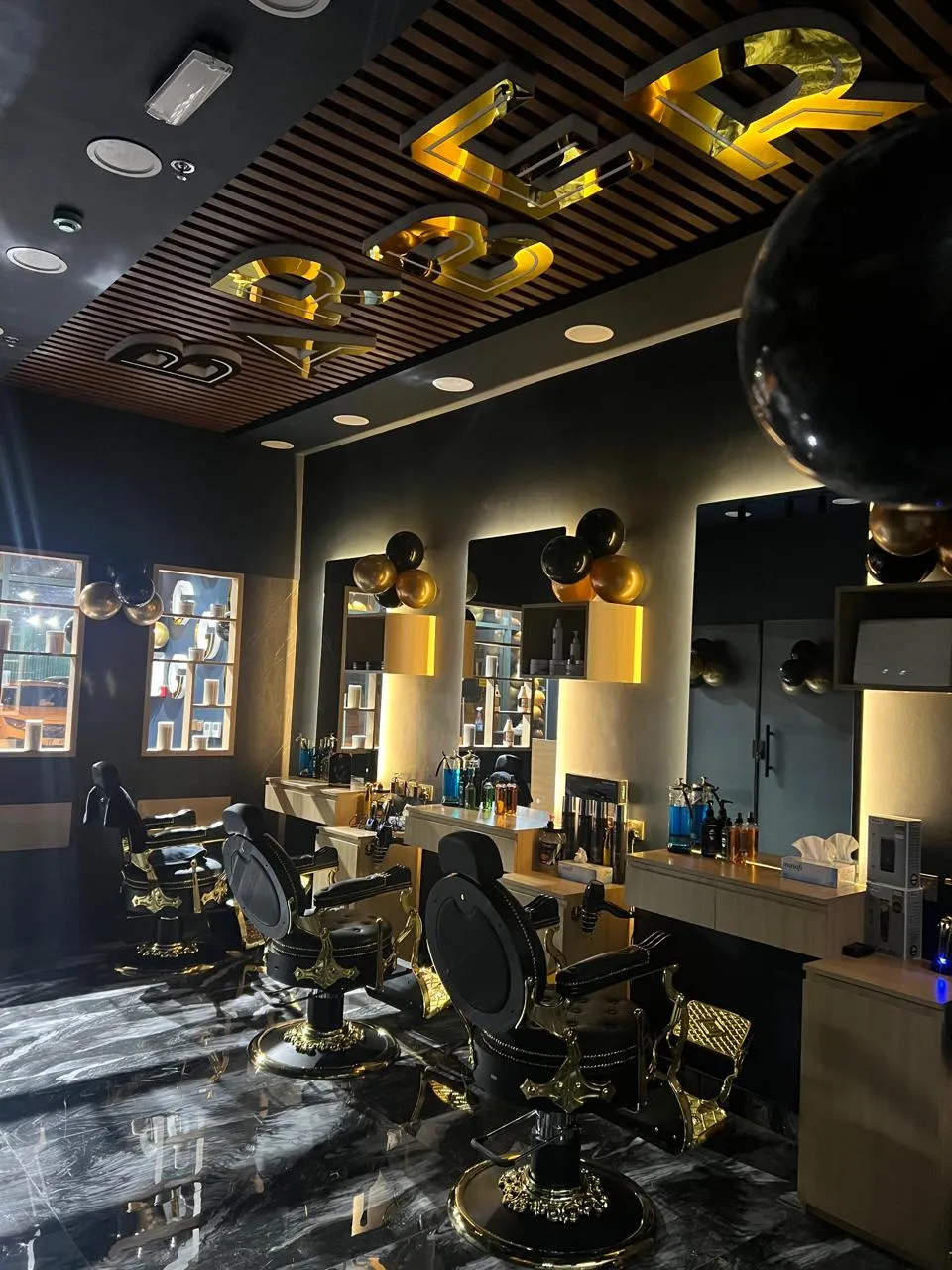 The three barber chairs under the gold BARBER lettering, reflected in the marble floor
